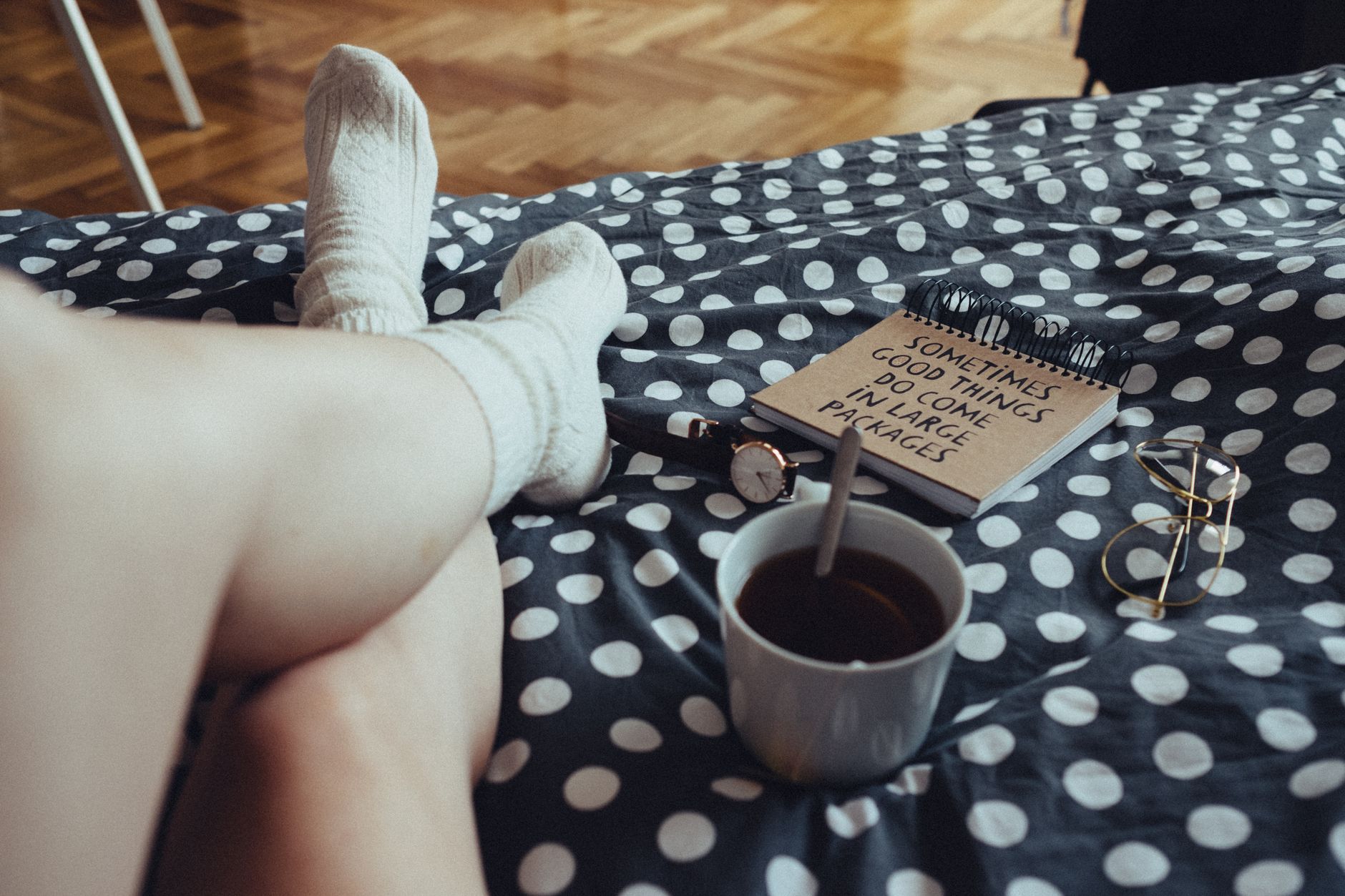 Person relaxing with tea, notebook, and polka dot bedding, creating a cozy atmosphere indoors.