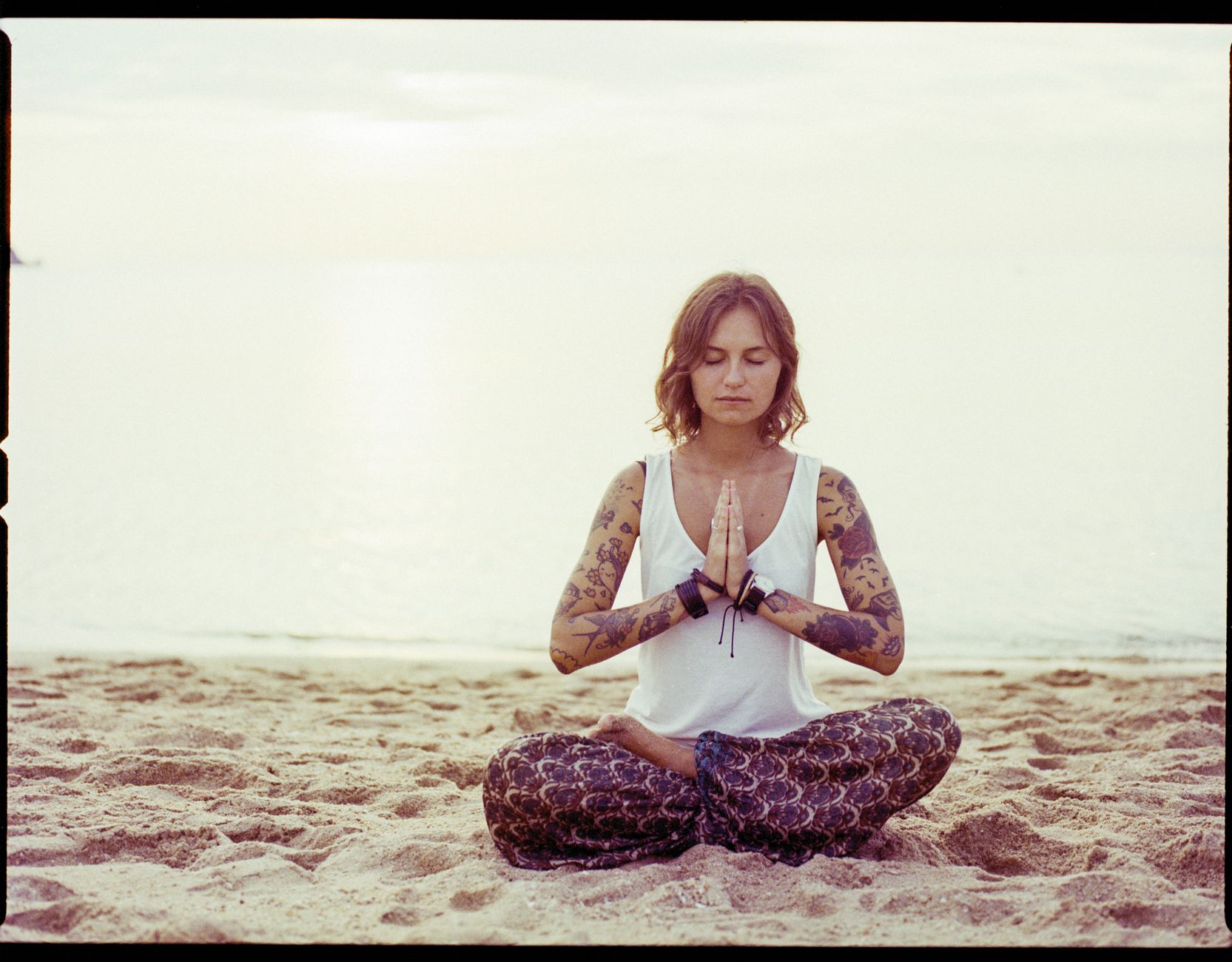 A woman practicing yoga meditation on a tranquil beach at sunrise.