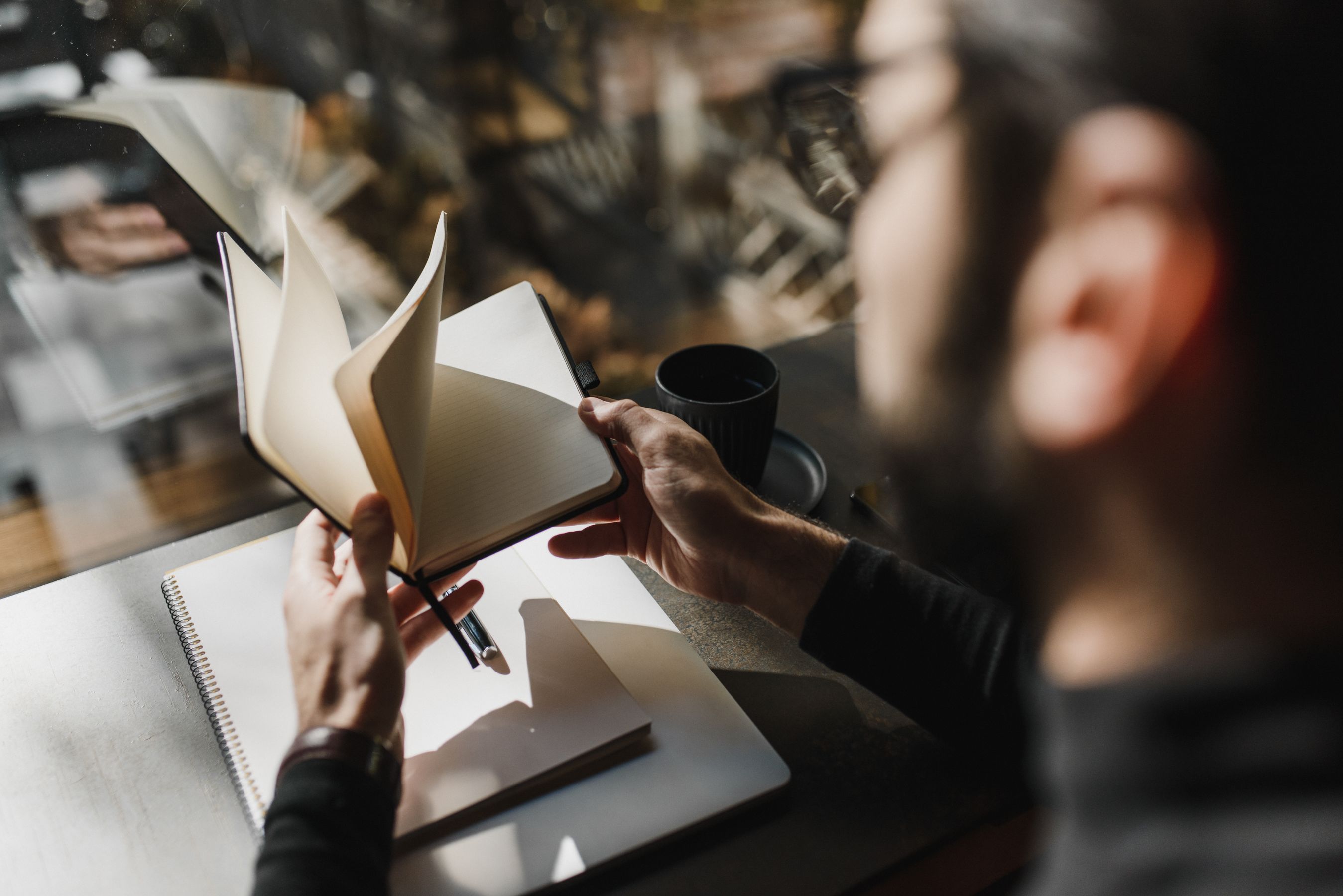 A person turning the pages of a notebook by a window.
