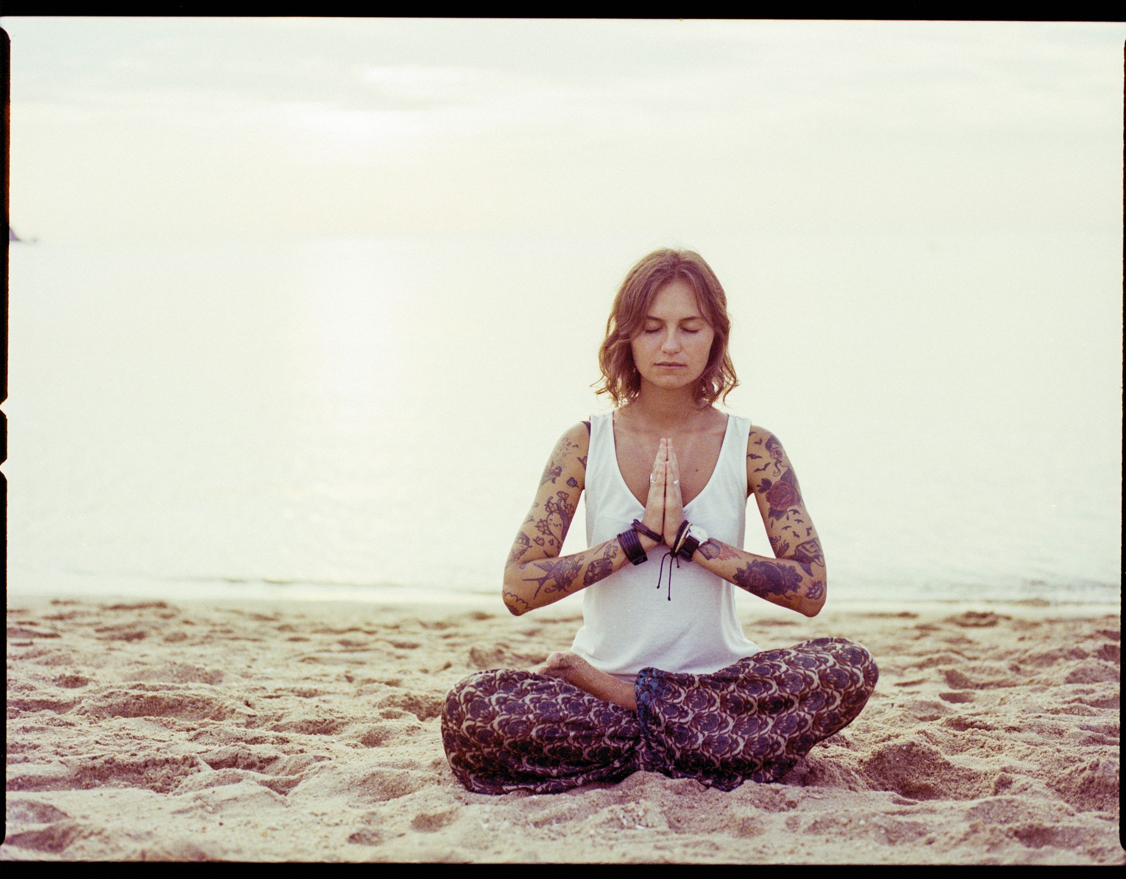 A woman practising yoga on a quiet beach at sunrise.