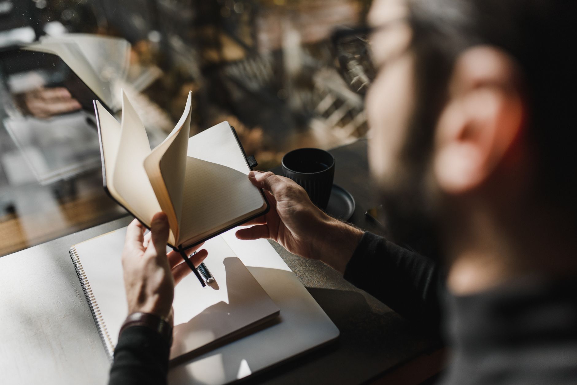 A person flipping through a notebook by a window.